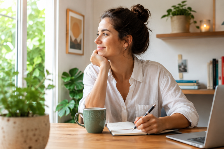 Mujer en su espacio de trabajo trabajando y pensando alegremente mientras mira por la ventana.