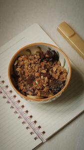 Bol de cereales y frutos secos sobre un cuaderno de notas durante una rutina de mañana productiva.